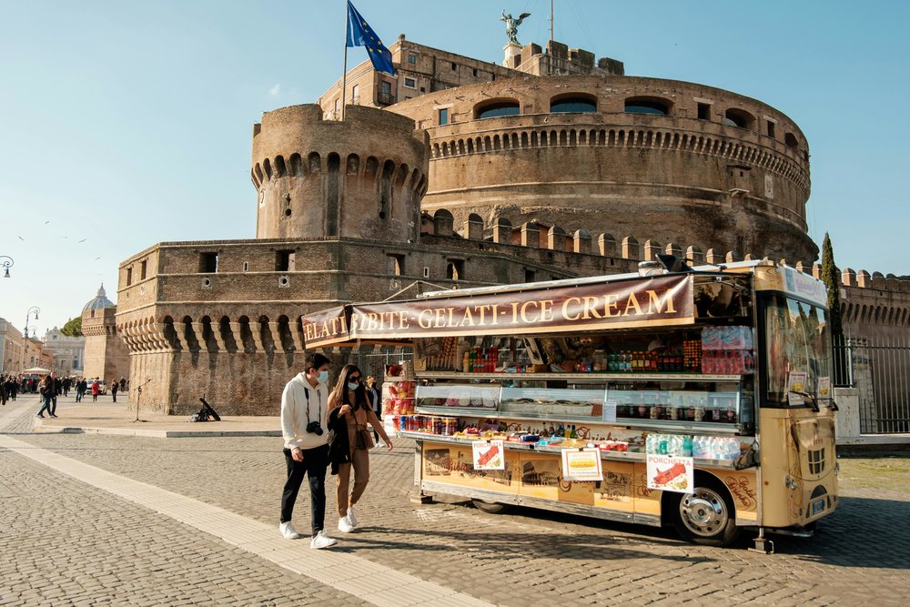 A gelato cart in front of the Castel Sant'Angelo with people walking by and enjoying their ice cream | Photo Credit: Matteo Basile on Pexels