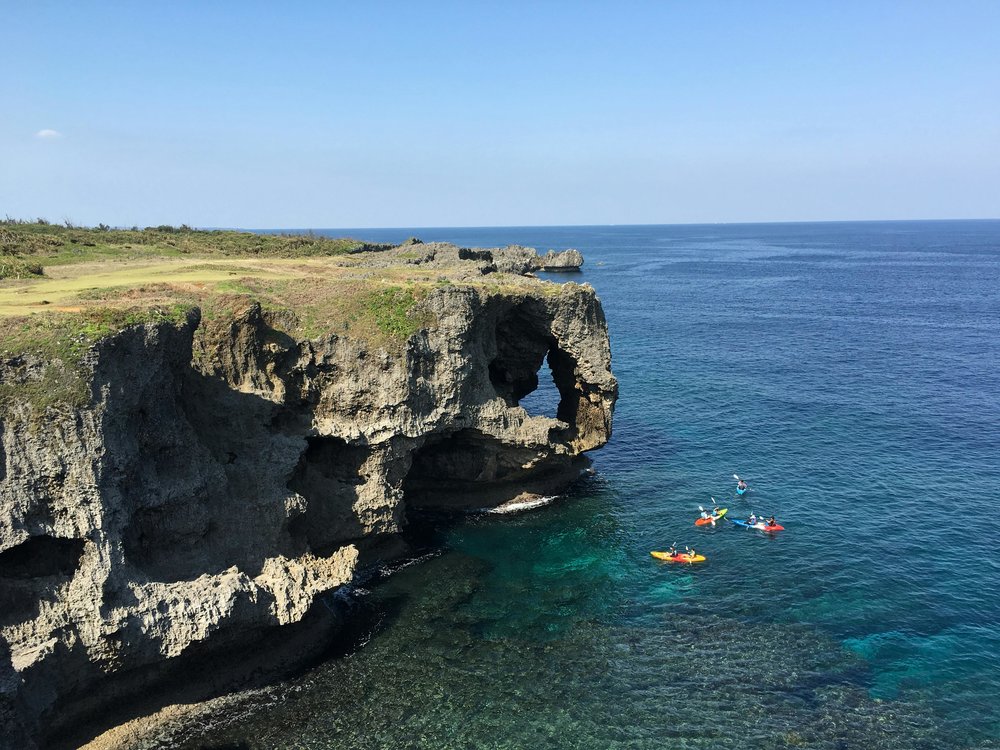 Rocky cliff arch at Cape Manzamo above blue sea | Photo Credit: Robert Yang on Unsplash