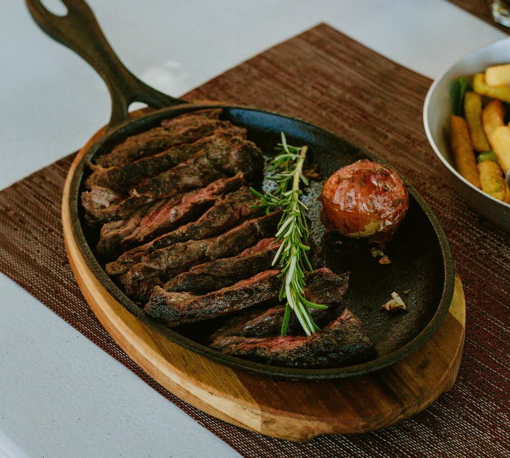 A sizzling flat iron steak with rosemary and roasted vegetables on a cast-iron plate