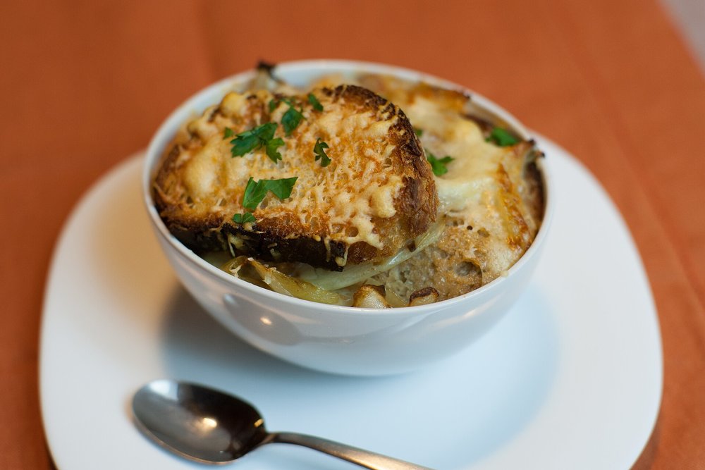 Bowl of French onion soup with cheese toast, garnished with fresh herbs