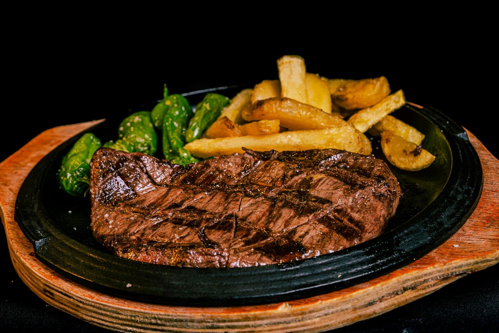  A sizzling rib-eye steak on a hot plate with potatoes and grilled peppers