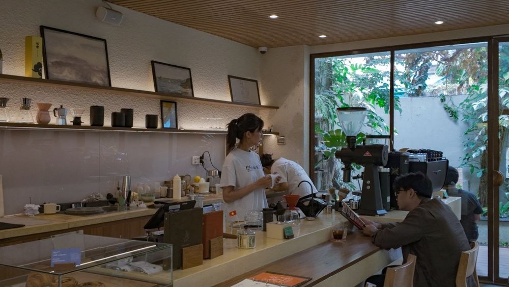 A barista behind a coffee shop counter and a customer reading a book