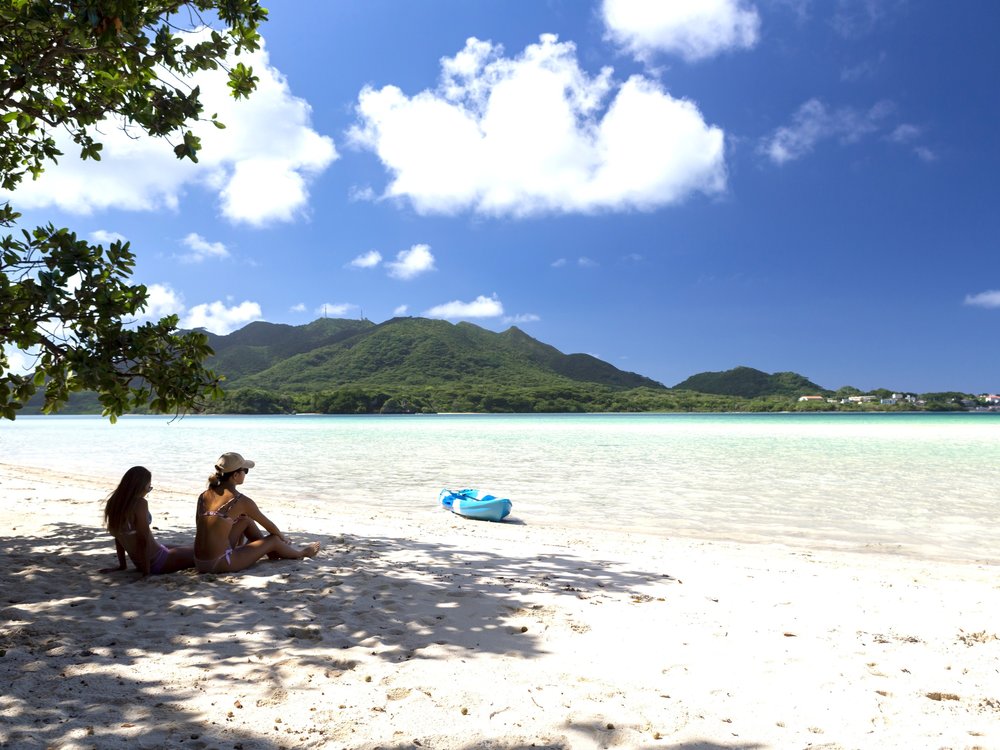 Two women sitting on white sand beach in Okinawa