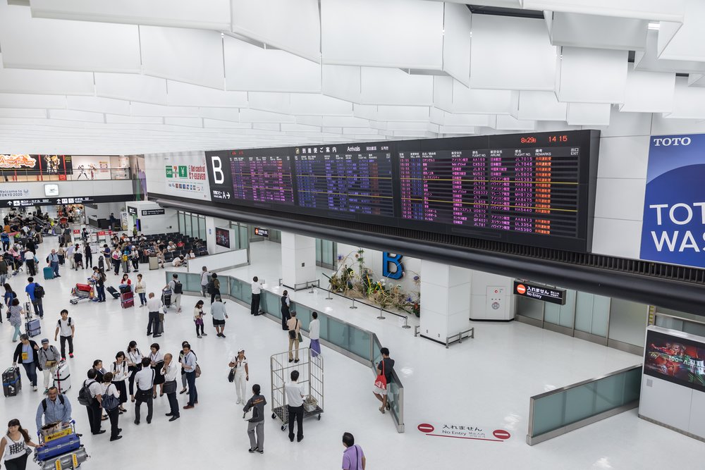 Arrival hall in a Japanese airport with travelers and flight information board