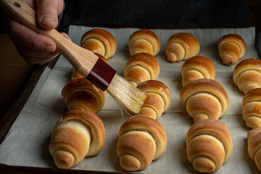 Brushing butter on a batch of croissants