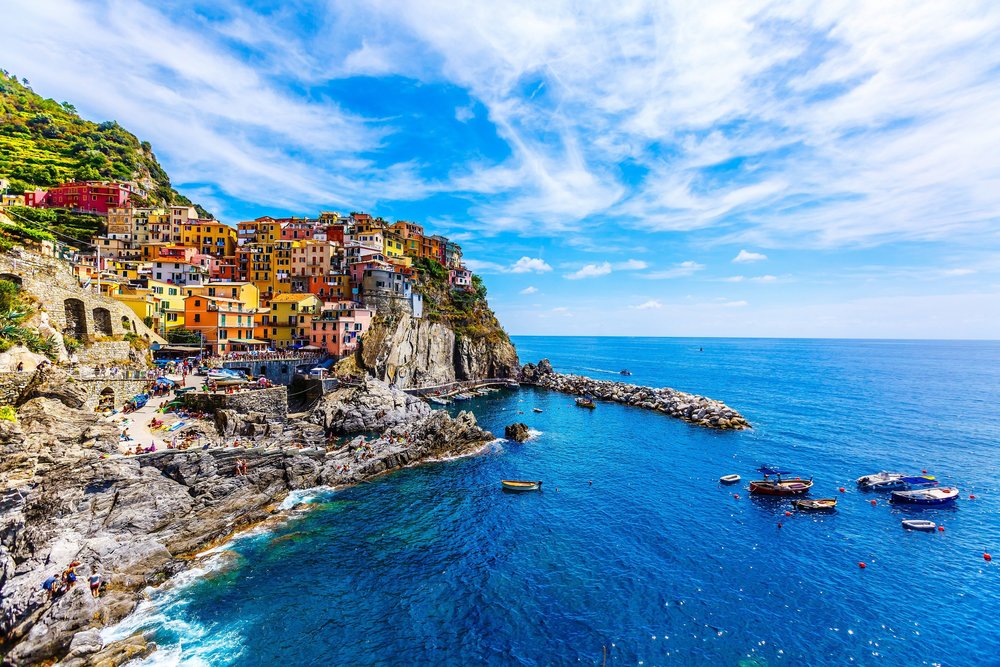 A cliffside covered with colorful buildings next to a body of water with rocks and boats.