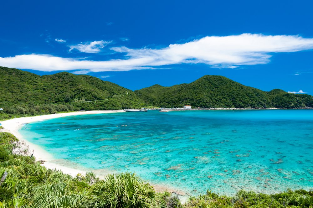 Scenic view of Aharen Beach with clear blue water and green hills in Okinawa
