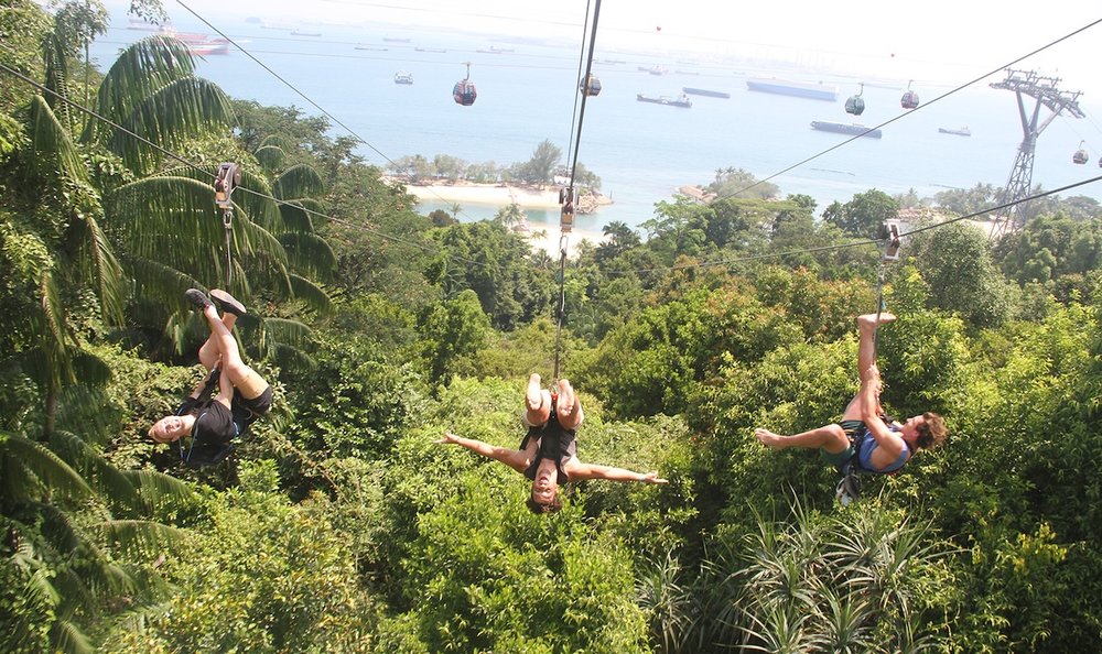 3 people ziplining at Sentosa Island overlooking the ocean