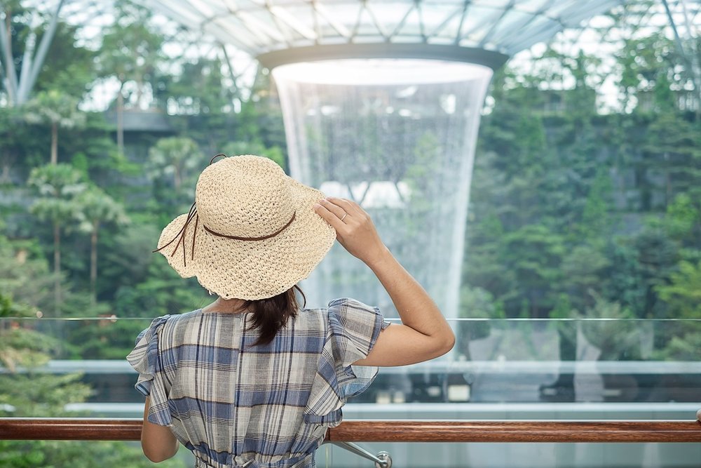 A woman in a straw hat overlooks the HSBC Rain Vortex and Shiseido Forest Valley at Jewel Changi Airport.