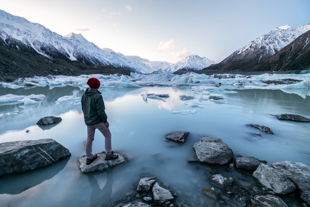 Traveler exploring icy glacier lake surrounded by snow-capped mountains in winter