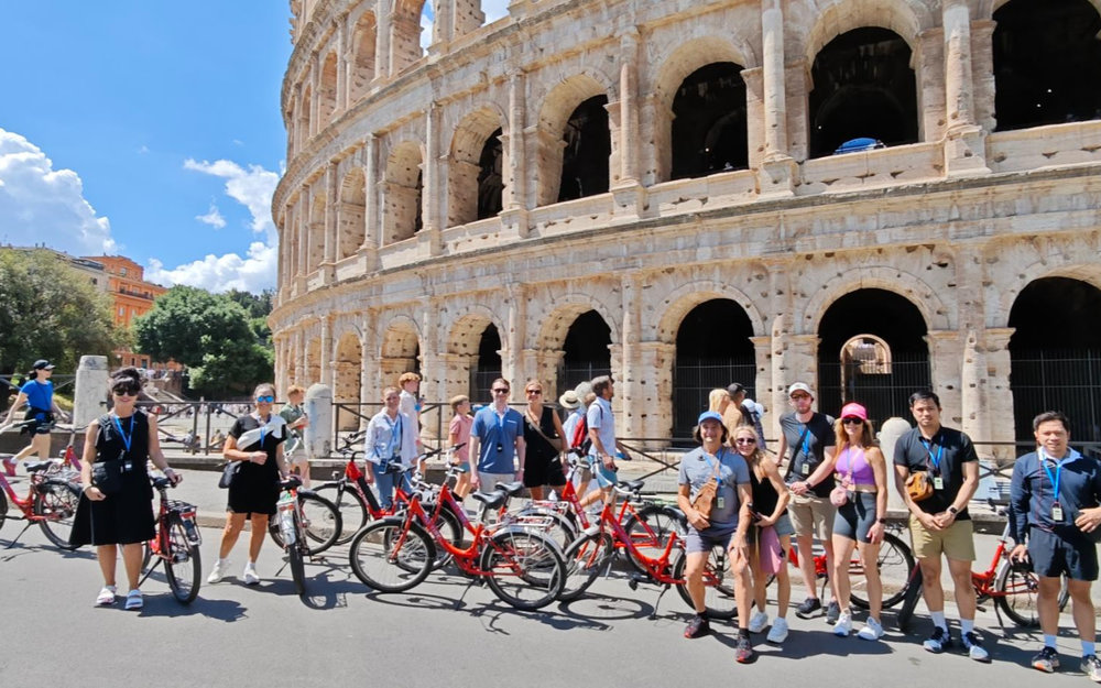 Different people with bikes posing in front of The Colosseum