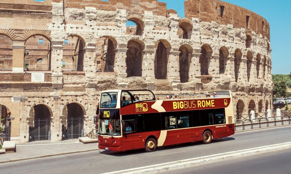 A big red bus in front of a giant amphitheater structure in the daytime
