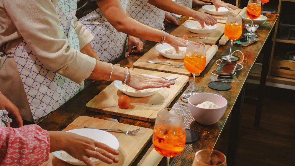 Five people reaching into individual bowls of flour on wooden trays next to glasses of orange-colored liquid.