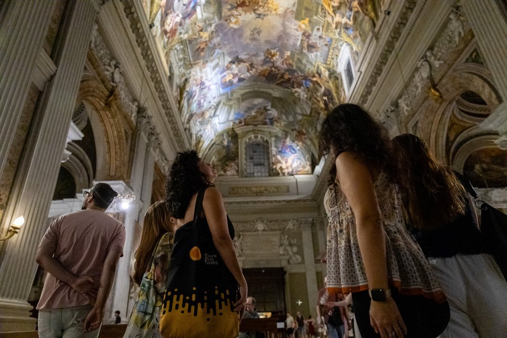 A group of five people looking up at a large painted ceiling in a gothic style building