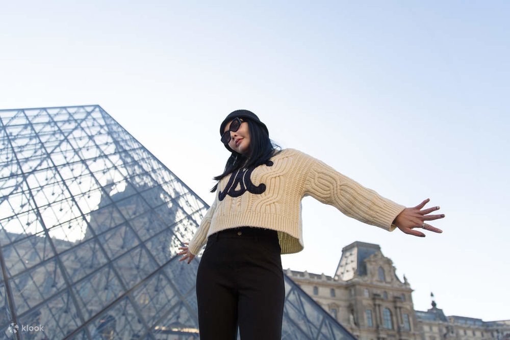 A woman posing in front of the Louvre.