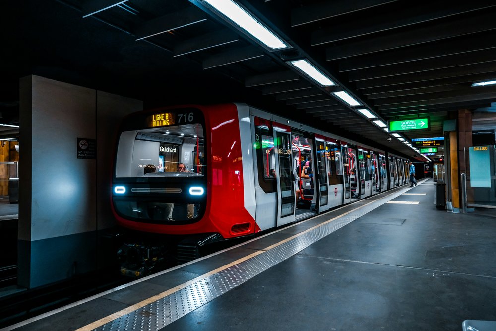 A red and gray underground train in a dim station with large overhead lights.