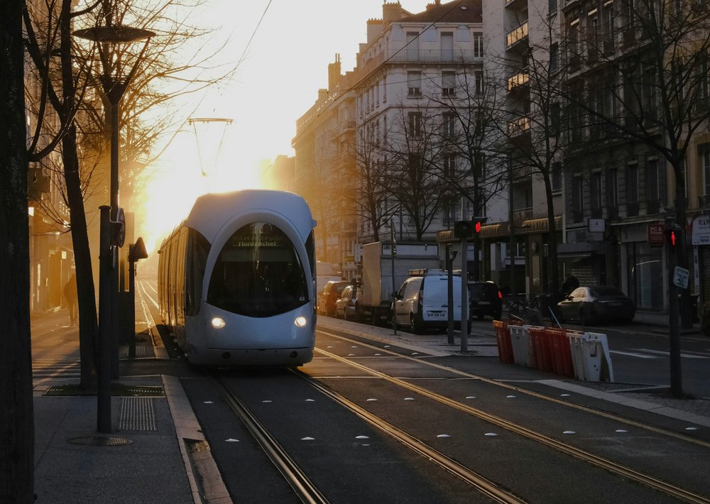 A white tram rolling into an empty street against a sunrise