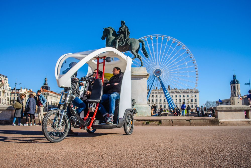 Two people in a pedicab in front of a statue of a horserider and a ferris wheel.