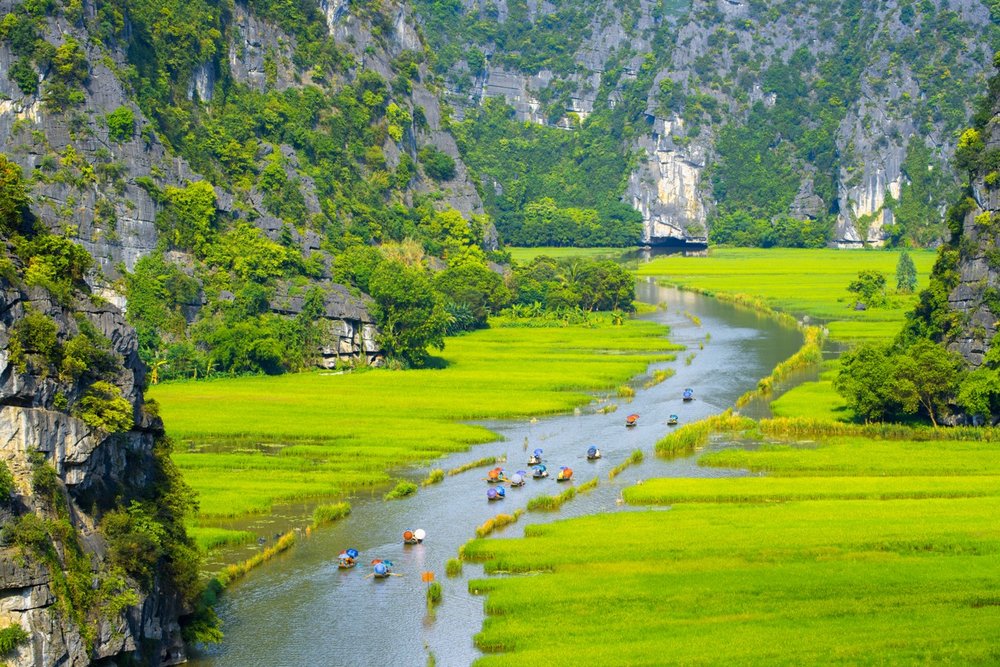 A river valley in between greenery and mountains with people on boats in the water.
