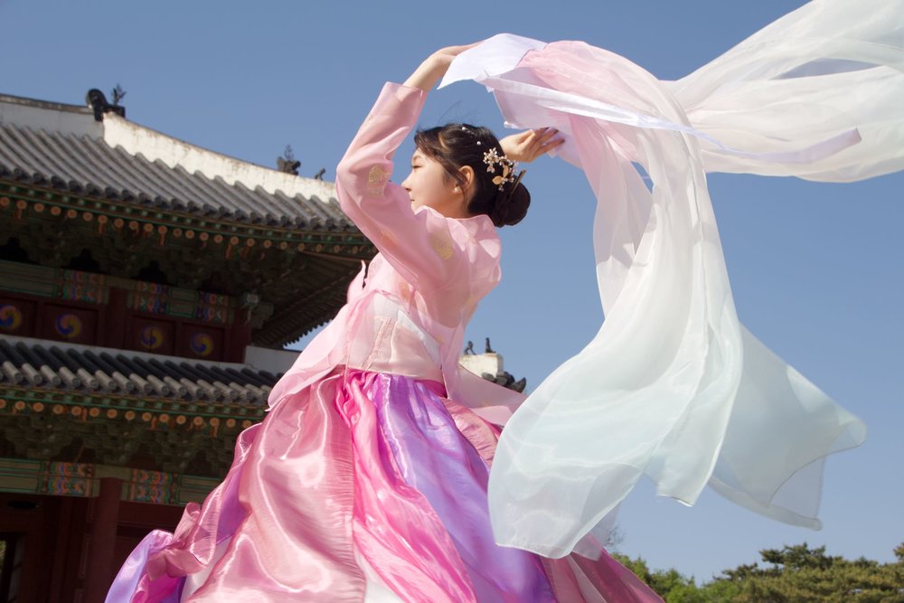 Woman in pink hanbok posing in front of Gyeongbokgung Palace under a clear sky