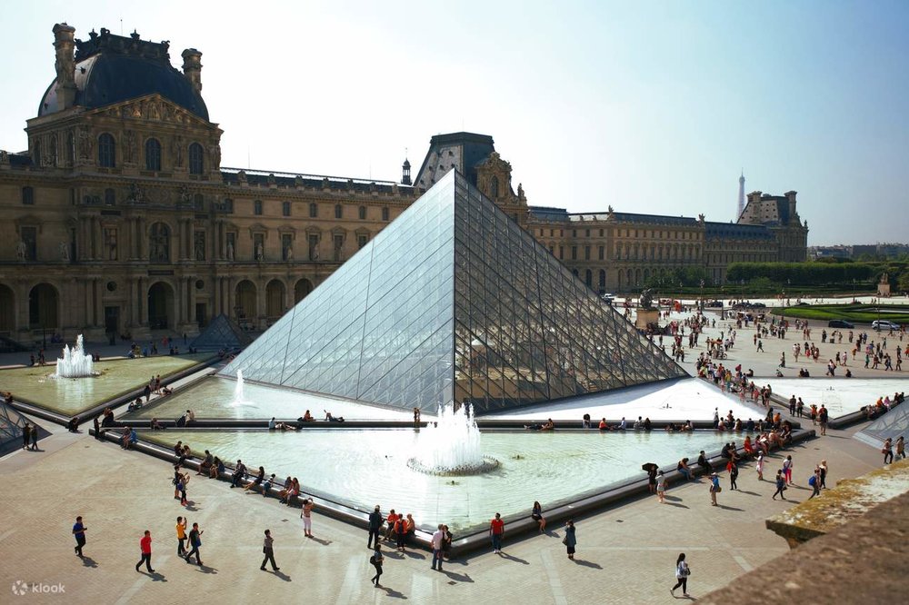 A crowd of people outside the Louvre, where the Louvre Pyramid stands