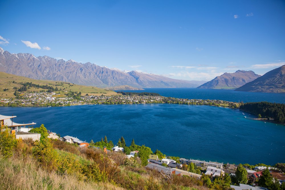 A large body of water surrounded by mountains, trees, bushes, and scattered houses.