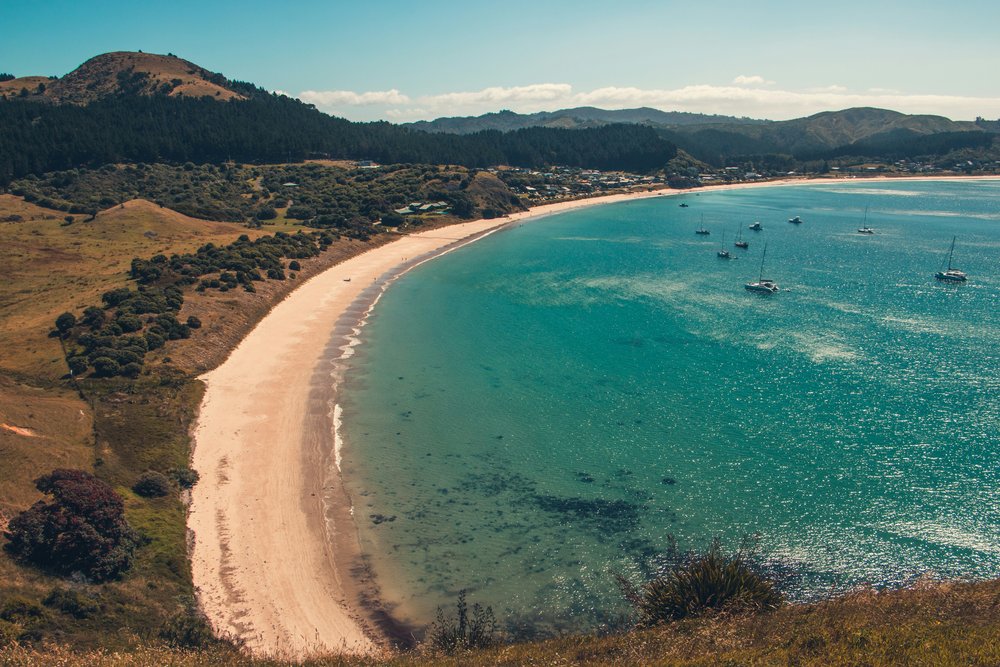 A curved beach next to tree-covered land and mountains.