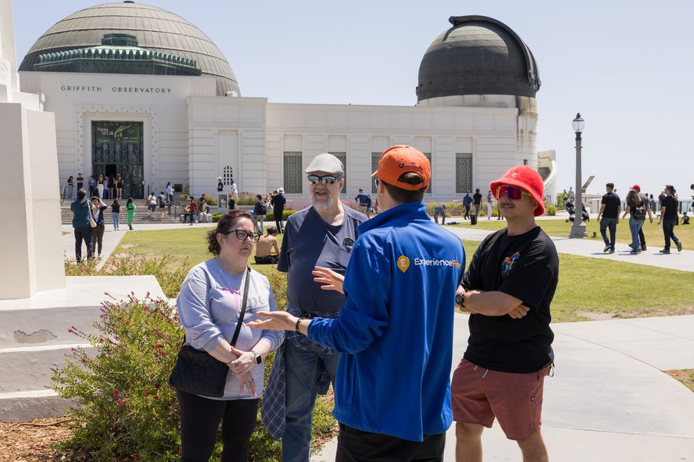 A group of people stands in front of Griffith Observatory while a guide talks to them outdoors