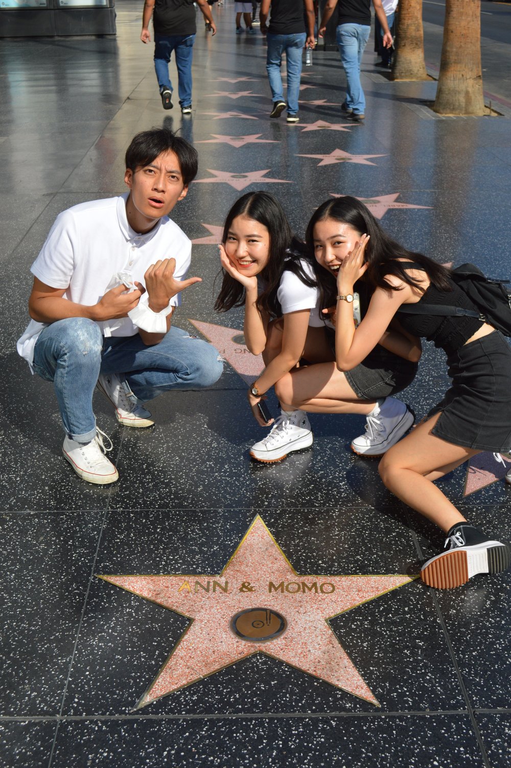 Three friends crouch and pose beside a star on the Hollywood Walk of Fame along the sidewalk