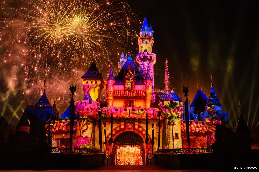 Disneyland castle glowing with colorful lights as fireworks burst in the night sky behind it