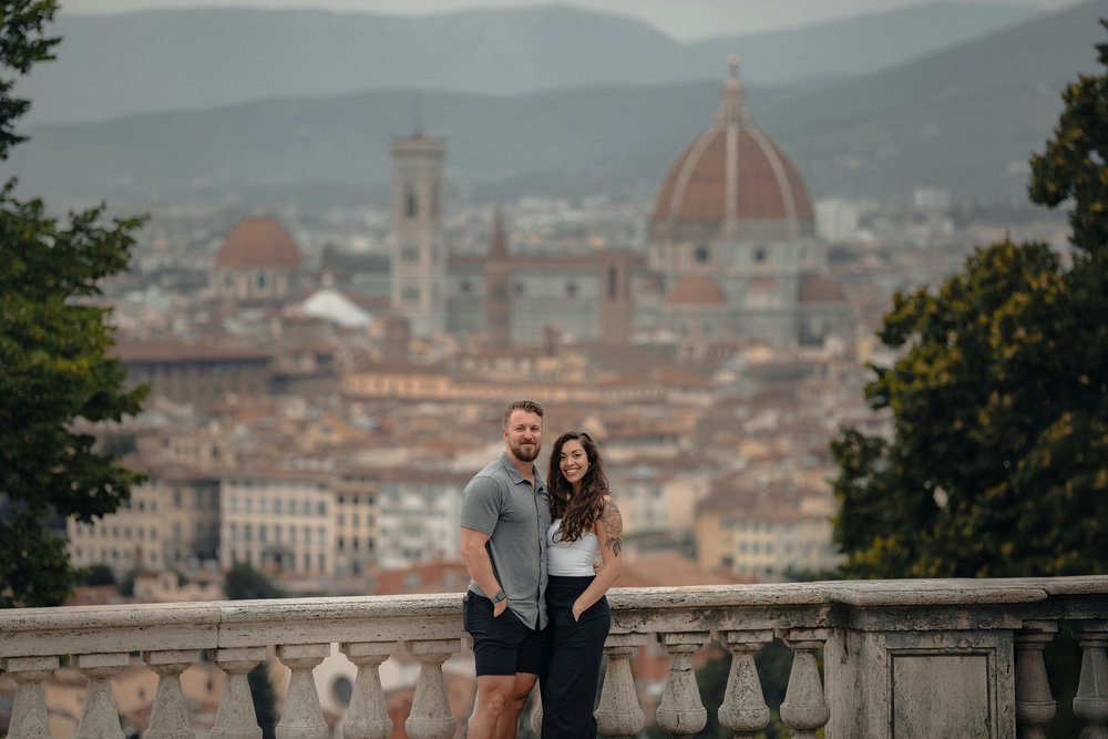 A couple dressed in light, smart-casual clothing posing with the Florence skyline in the background
