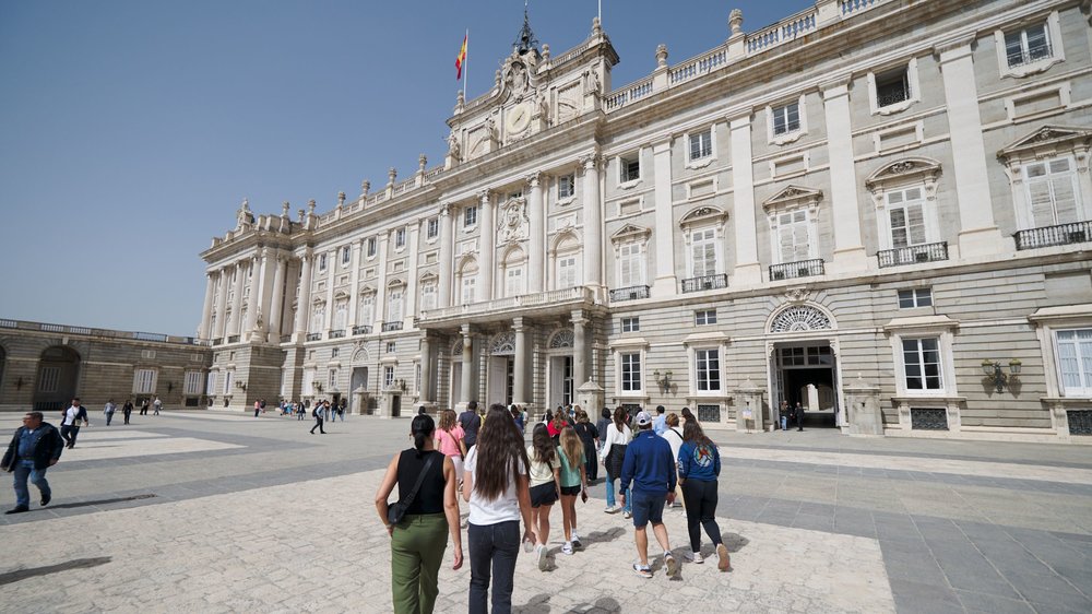 A wide shot of the majestic Royal Palace of Madrid with its large courtyard and Spanish flag