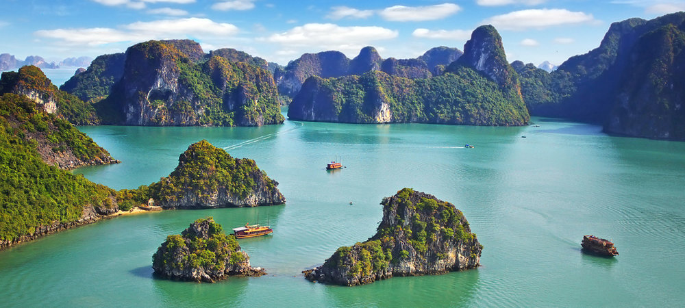 Halong Bay with emerald water, limestone karsts, green islands, and cruise boats under a blue sky