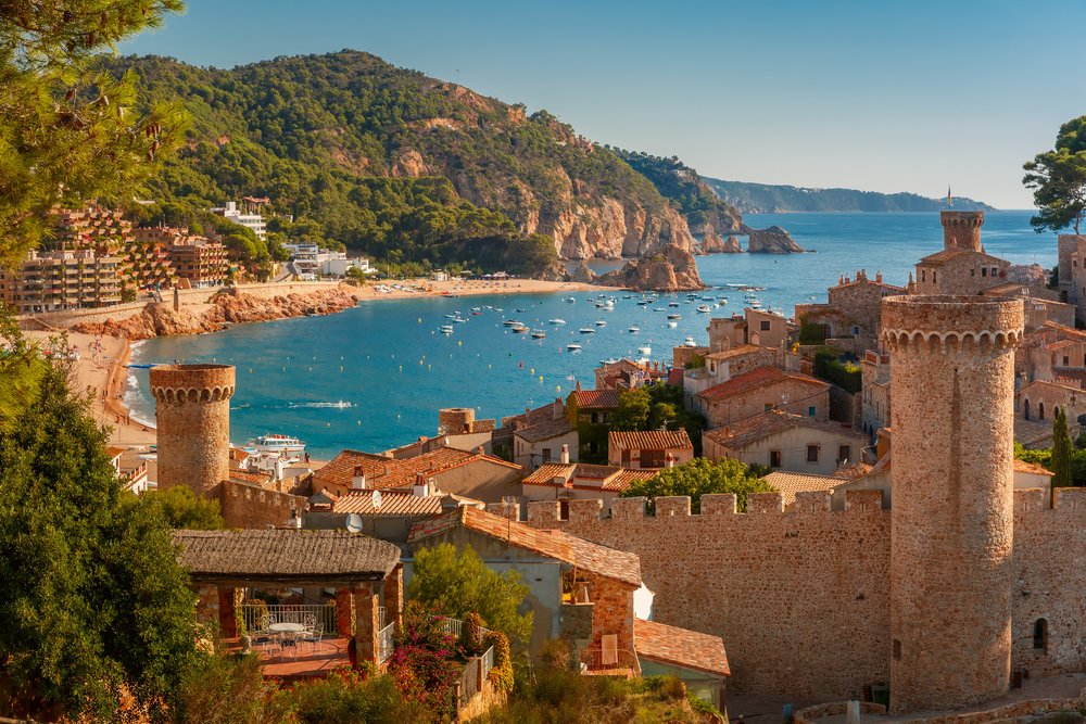 Coastal view of Costa Brava with turquoise water, boats, and a historic seaside village