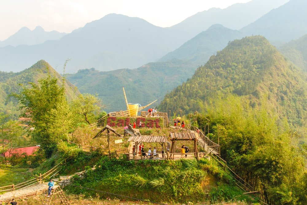 Green rice terraces carved into the steep mountainsides of Sapa, with a village visible in the valley below.