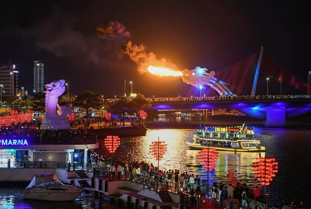 The Dragon Bridge in Da Nang illuminated at night, with crowds gathered to watch the fire and water show.