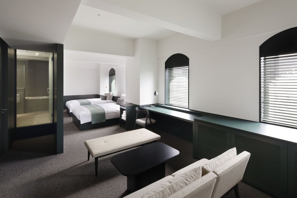 A spacious room, with a small couch set on one side and two beds on the other