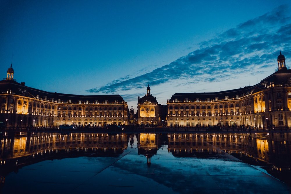 Illuminated Place de la Bourse reflected in water at dusk in Bordeaux | Photo Credit: Audiala
