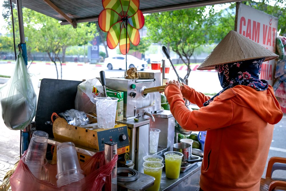 Street vendor preparing sugarcane juice at outdoor cart with various ingredients