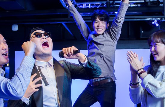 Two men and a woman happily posing for a photo with PSY's wax figure