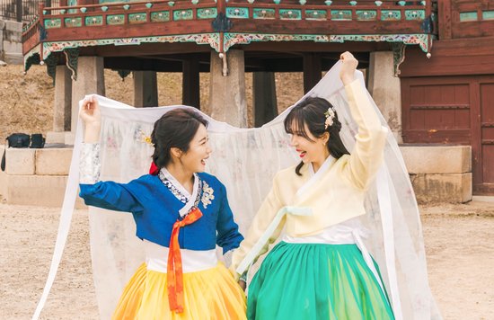 Two ladies wearing traditional hanboks while happily smiling at each other