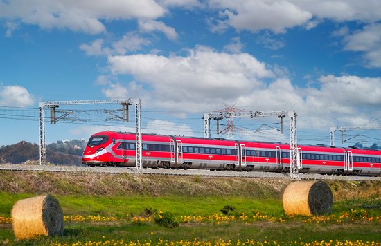 Red Trenitalia Frecciarossa train passing by fields and hills in Italy