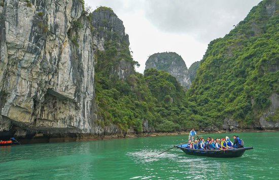 Tourists on a bamboo boat surrounded by towering limestone cliffs in Halong Bay