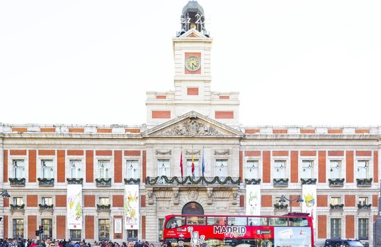 Red sightseeing bus in front of Puerta del Sol building in Madrid