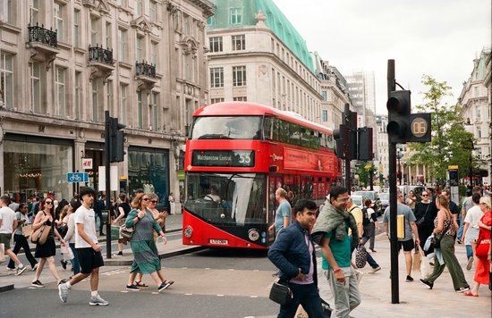 Red double-decker bus passing through a busy London street with pedestrians crossing | Photo Credit: Intrepid on Unsplash