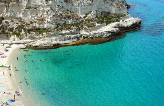 An aerial shot of a large, turquoise body of water and a small shore full of people Photo from Pixabay