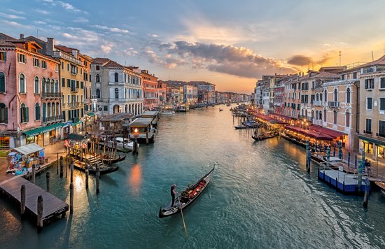 Gondola cruising the Grand Canal at sunset with glowing city lights