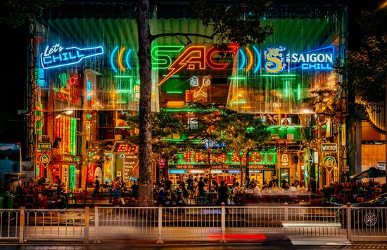 Busy nightlife street in Ho Chi Minh City with neon bar signs and crowds enjoying drinks at night