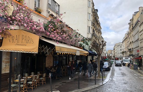 A scenic street in Montmartre with a café and blooming flowers overhead