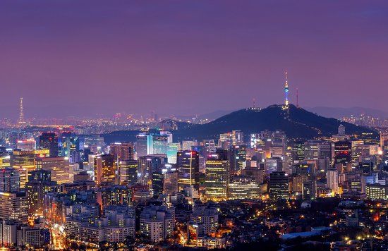A wide shot of illuminated buildings and towers against a purple sunset